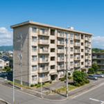 徳島市内の住宅街に建つ築40年程度の老朽化した分譲マンション。青空を背景にしたマンション解体検討時期の建物外観イメージ。