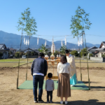 徳島での地鎮祭の様子。青空の下、更地で神主の祈祷に合わせ、後ろ姿で並ぶ家族が工事の安全を祈願する風景。