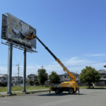 徳島県での看板撤去作業風景。青空の下、高所作業車を使用して老朽化した看板を安全に解体している様子。
