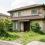 庭の草木が伸びて管理が必要な状態の、築30年ほどの2階建て日本家屋の外観