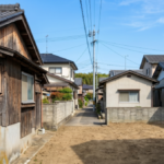徳島によく見られる住宅街の狭い路地で、解体工事後にきれいに整地された更地と青空の風景