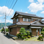 青空の下に建つ、徳島の典型的な木造2階建ての一軒家と周辺の住宅街の風景