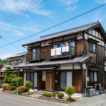 青空の下に立つ、木造2階建ての日本の住宅の写真。徳島県の特徴的な風景が描かれている。